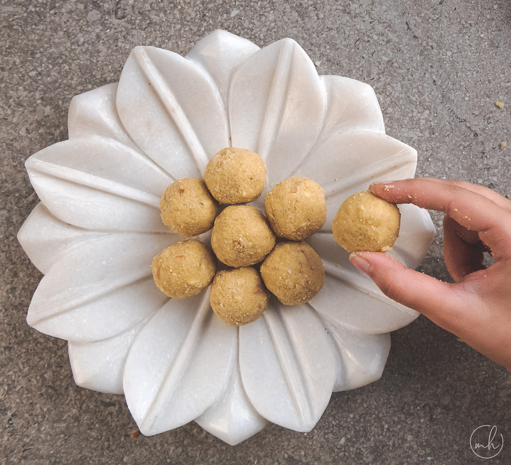 picking one whole wheat flour churma laddu placed on a white plate over a grey surface