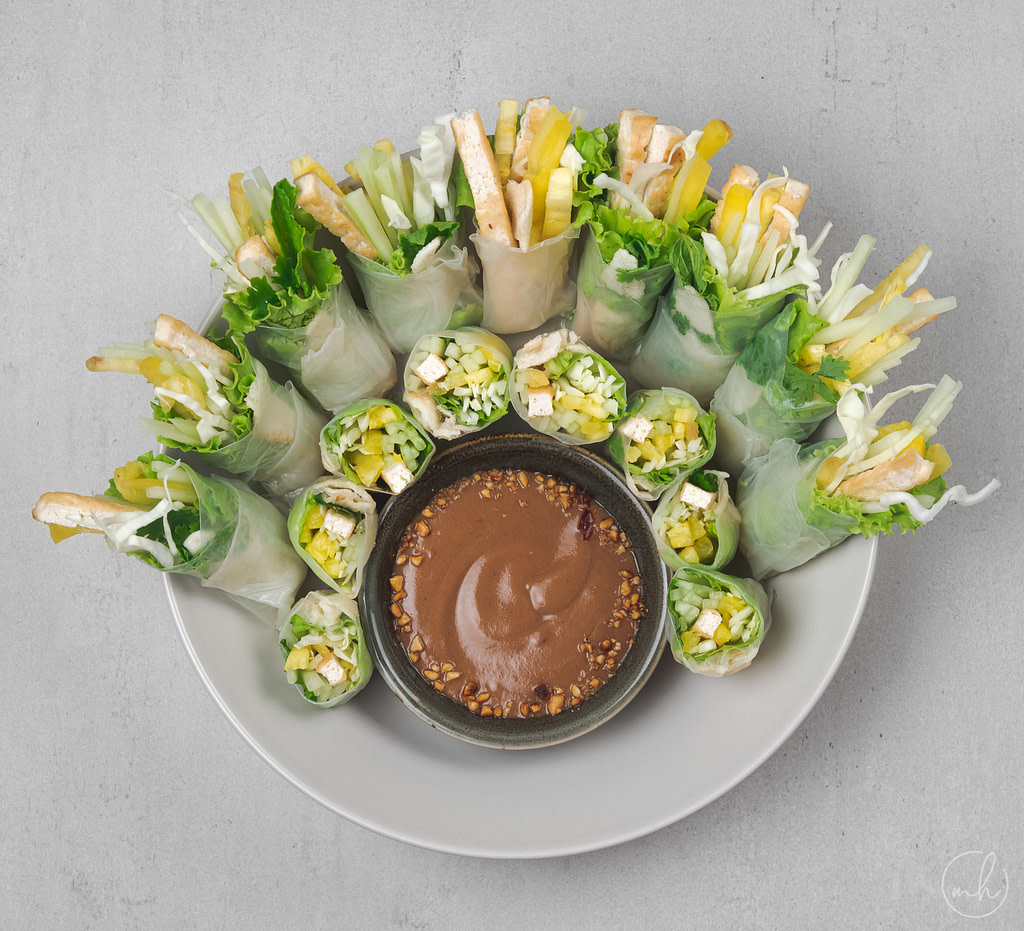 summer roll with tofu and pineapple placed in a bowl around peanut dipping sauce