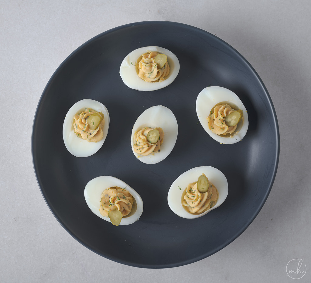 Deviled eggs with dill leaves and gherkins placed on a blue plate