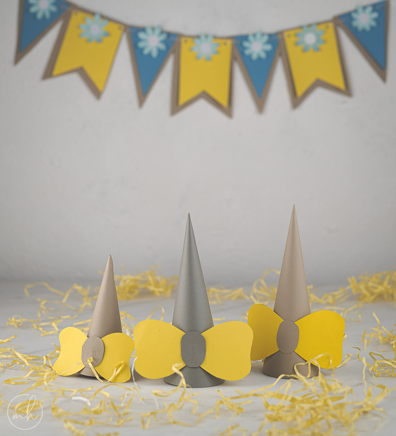 Gray-yellow bow party hats with scattered yellow fronds with blue-yellow party bunting in background