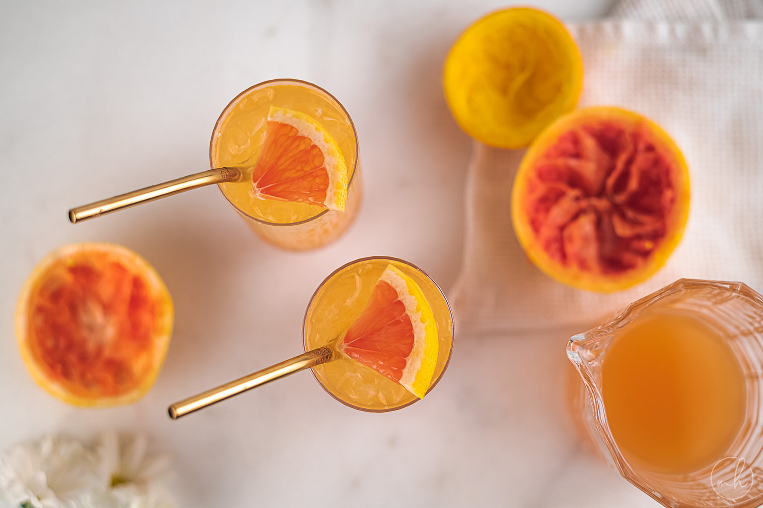 Two glasses of citrus riot juice with metal straws. Squeezed orange and grapefruit pieces with a jar of leftover juice is also placed.