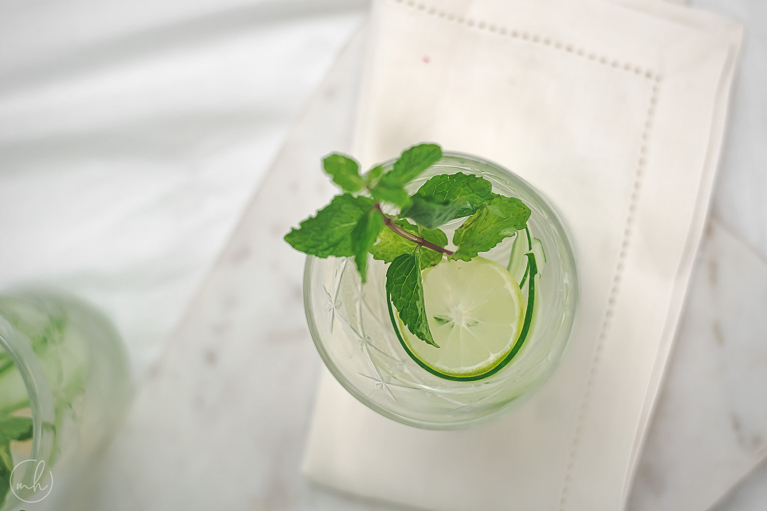 Focused, top view of a sliced lemon and cucumber peels, with the glass of cucumber basil lemonade in a blur.