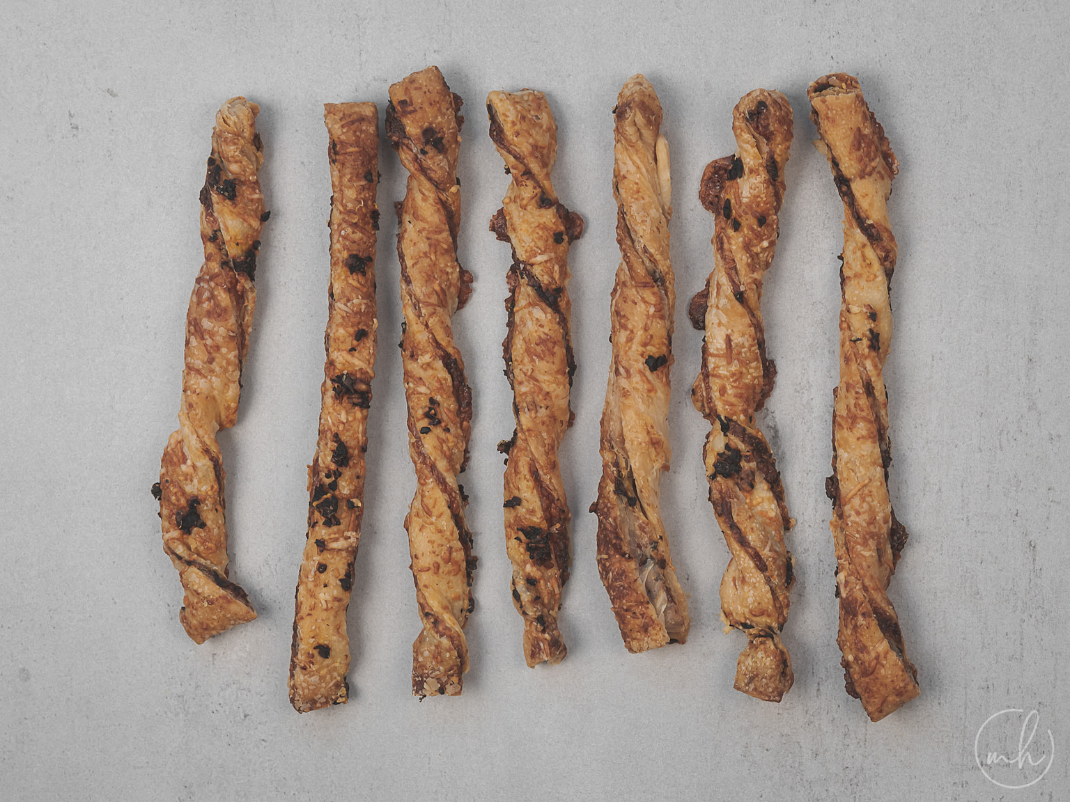 Sundried tomatoes and olive puff pastry cheese straws placed on a grey surface.