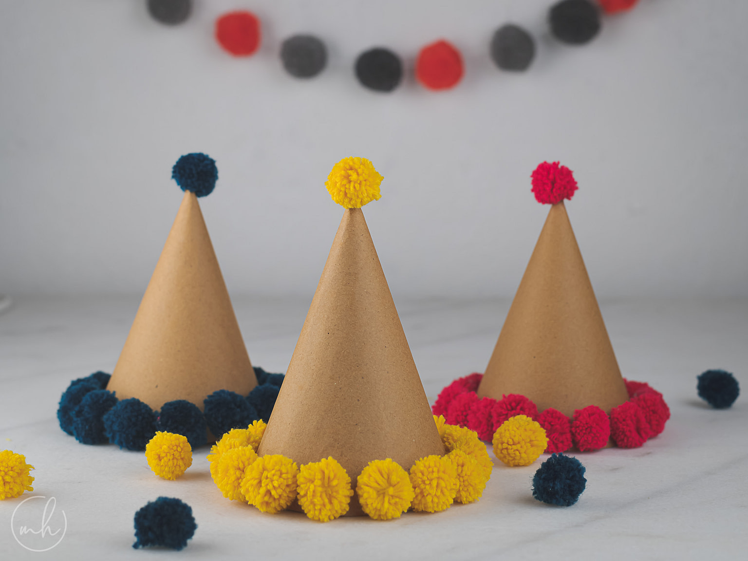 Colourful pompom party hats with red and black party banners in the background and scattered poms