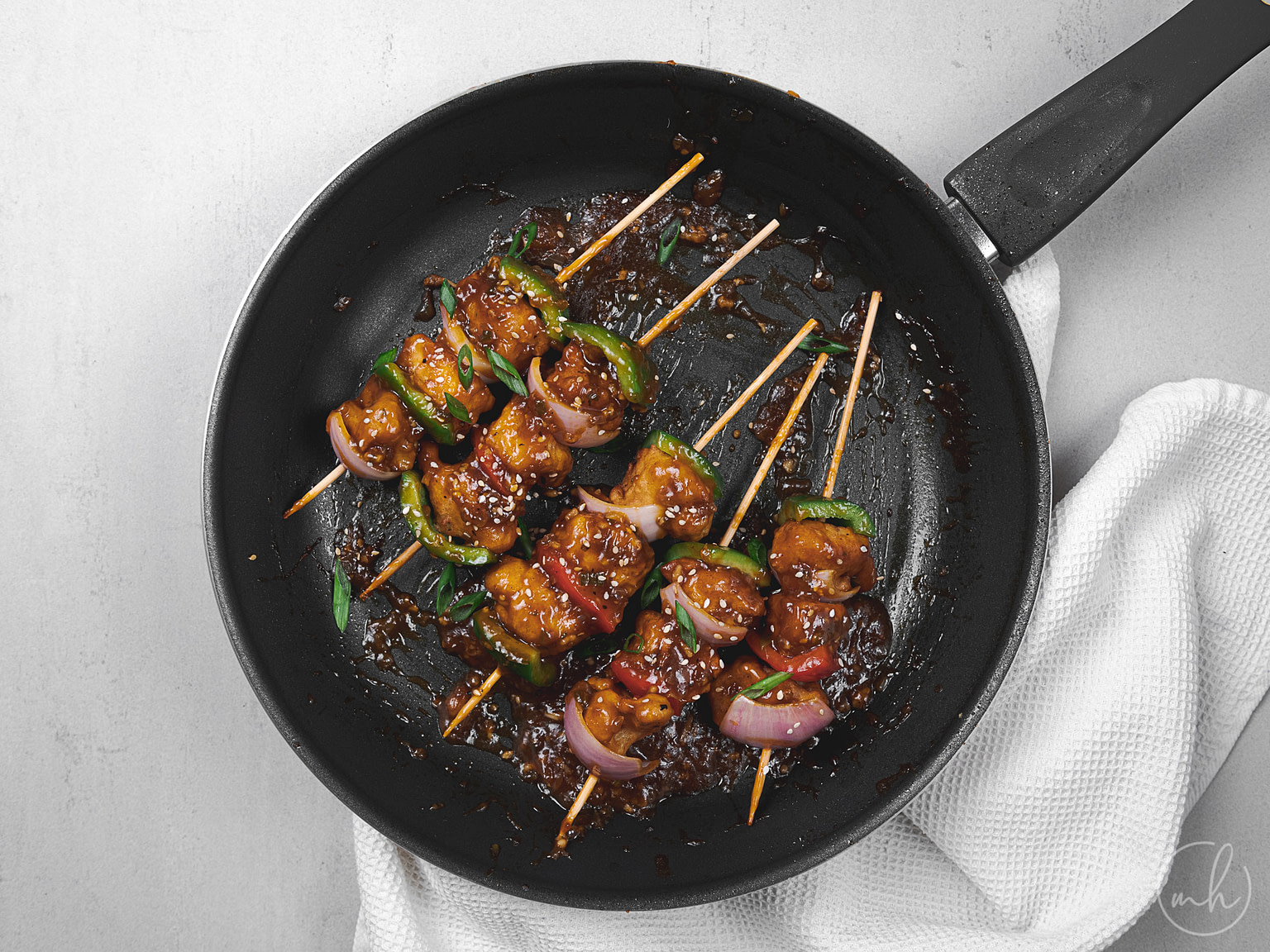 Cauliflower and paneer manchurian skewers in a pan, with a cloth underneath.