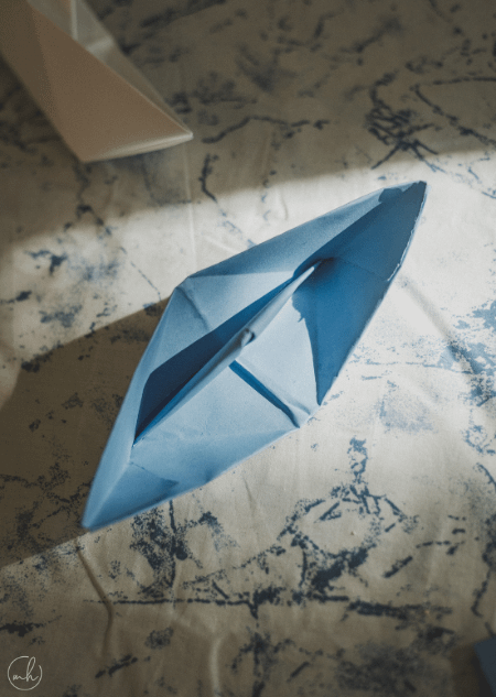 Kagazi: A blue colour paper boat and a white colour paper boat on a white and blue printed sheet