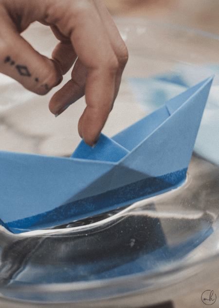 Kagazi: A hand playing with a blue colour paper boat