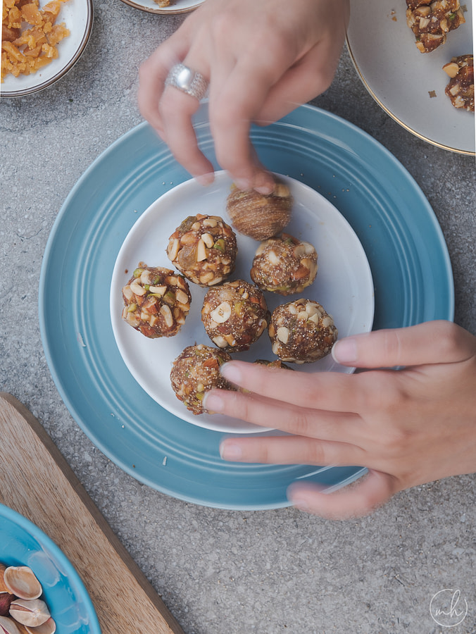 two hands placing the dates and dry fruit energy balls on a placed on a white plate under a blue rim plate