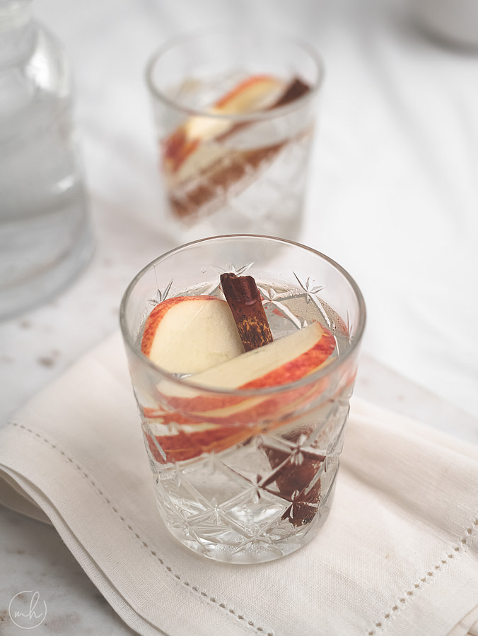 Close-up view of a glass filled with apple cinnamon infused water. It's placed on a marble tray with cloth napkin, with another glass in the background.
