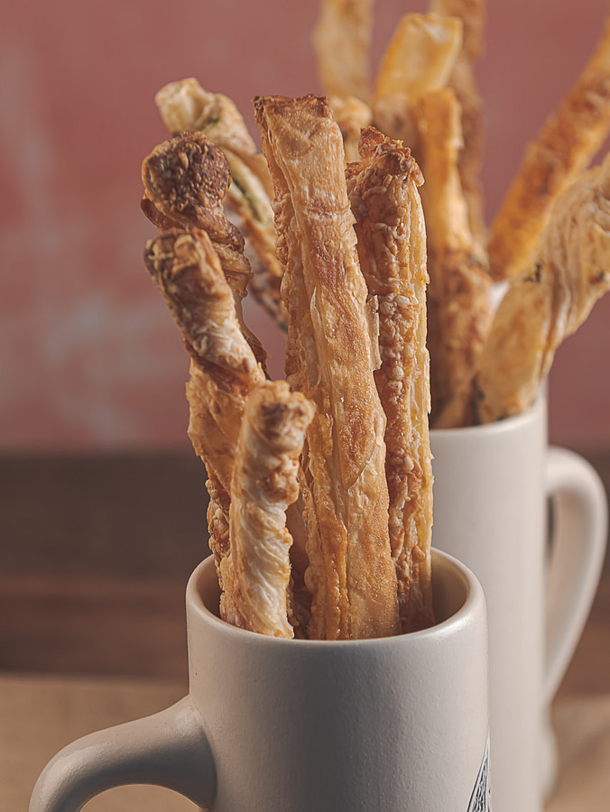 Herbed puff pastry cheese straws placed in a tea cup