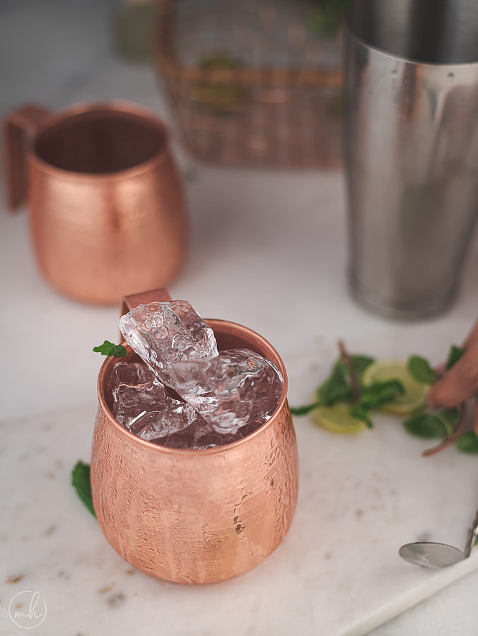 One copper mug of Moscow Mule placed on a marble tray with ice, lemon and fresh mint leaves as garnish.