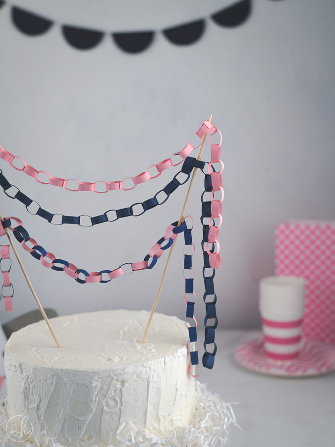 Pink-Blue paper chain cake toppers on white cake pink party crockery blue party banner in background