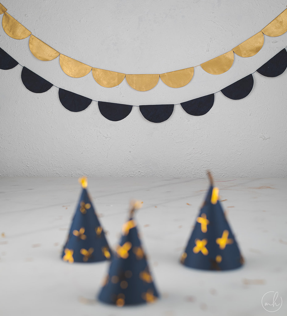 Blue party hats with golden glitter, scattered glitter and blue-gold party banners in the background
