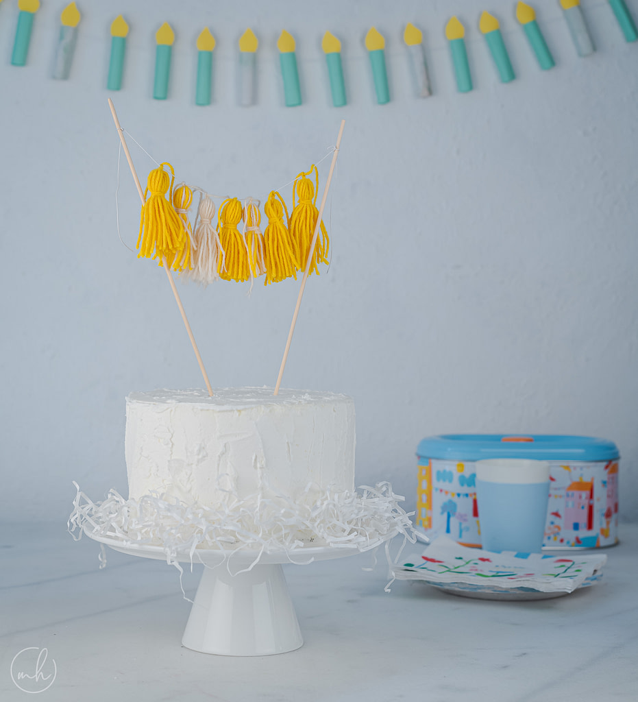 Yarn tassels cake topper on white cake with paper candle party banner party crockery in background